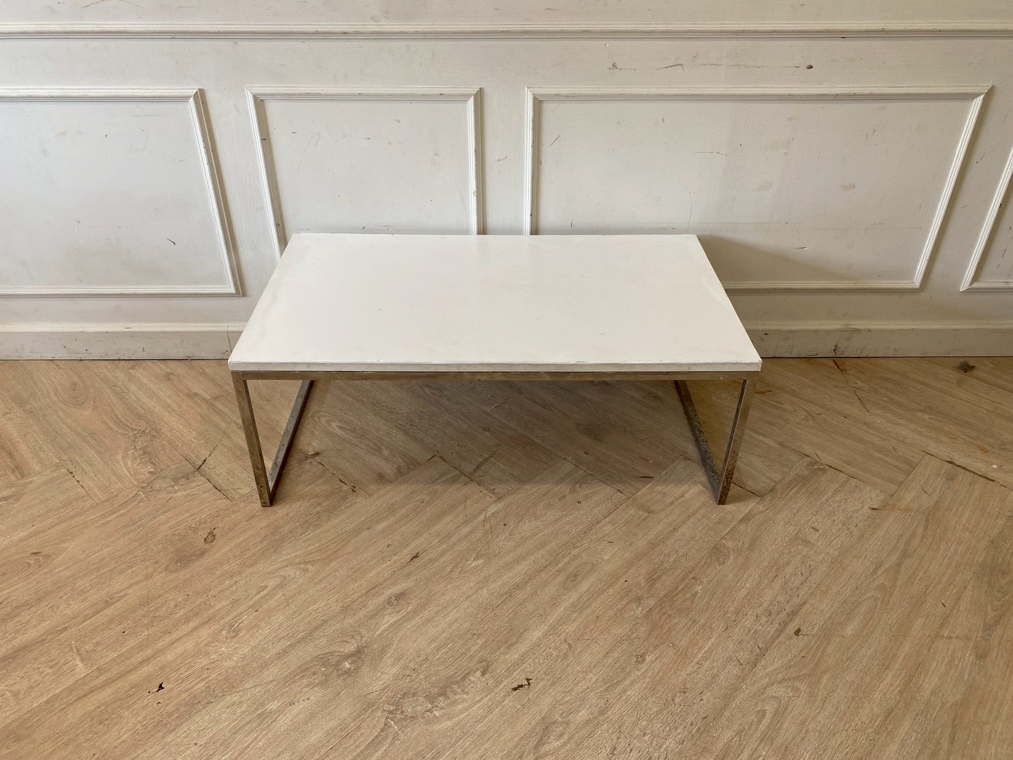 Coffee table with stainless steel legs and white wooden top.
